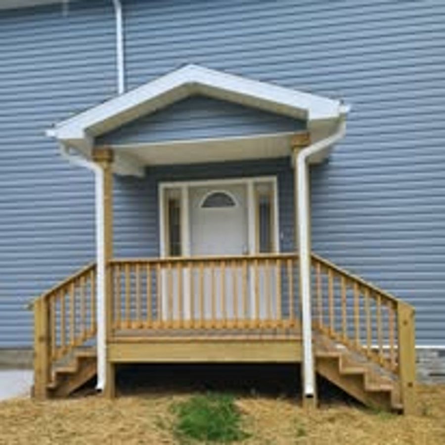 Covered entry portico with wooden steps and railing on a blue-gray sided home